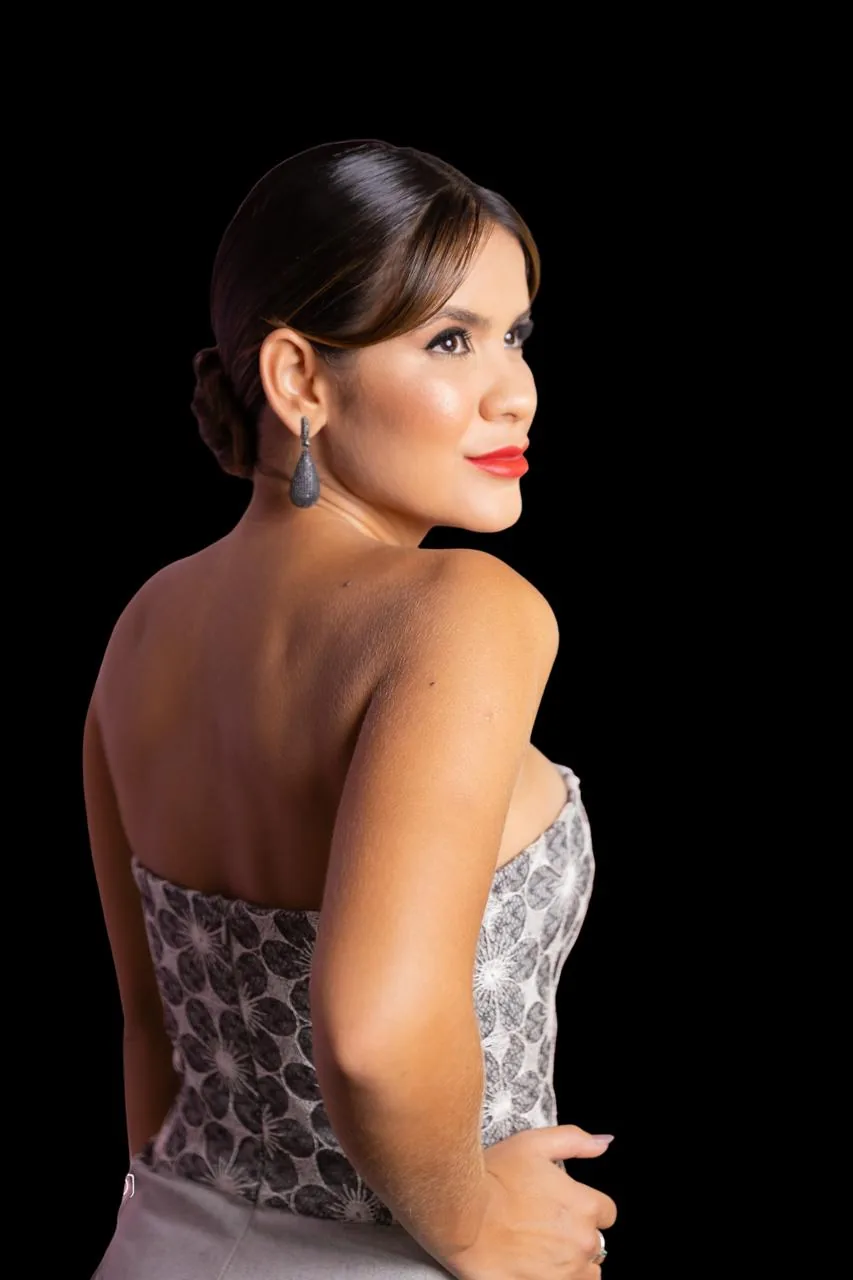 Retrato de Gabriella Moraes de perfil, com vestido tomara que caia estampado e brincos longos, sobre fundo escuro